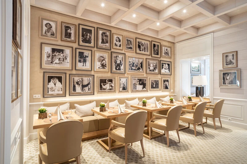 This elegant dining room in Hotel Sacher Salzburg features beige-toned decor, wooden furnishings, and a gallery wall adorned with black-and-white portraits of famous figures, creating a sophisticated yet cozy atmosphere.