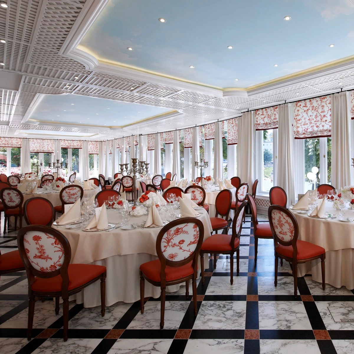 An elegant banquet hall at Hotel Sacher Salzburg with red and white decor, marble floors, and sky-blue ceilings set for a formal event.