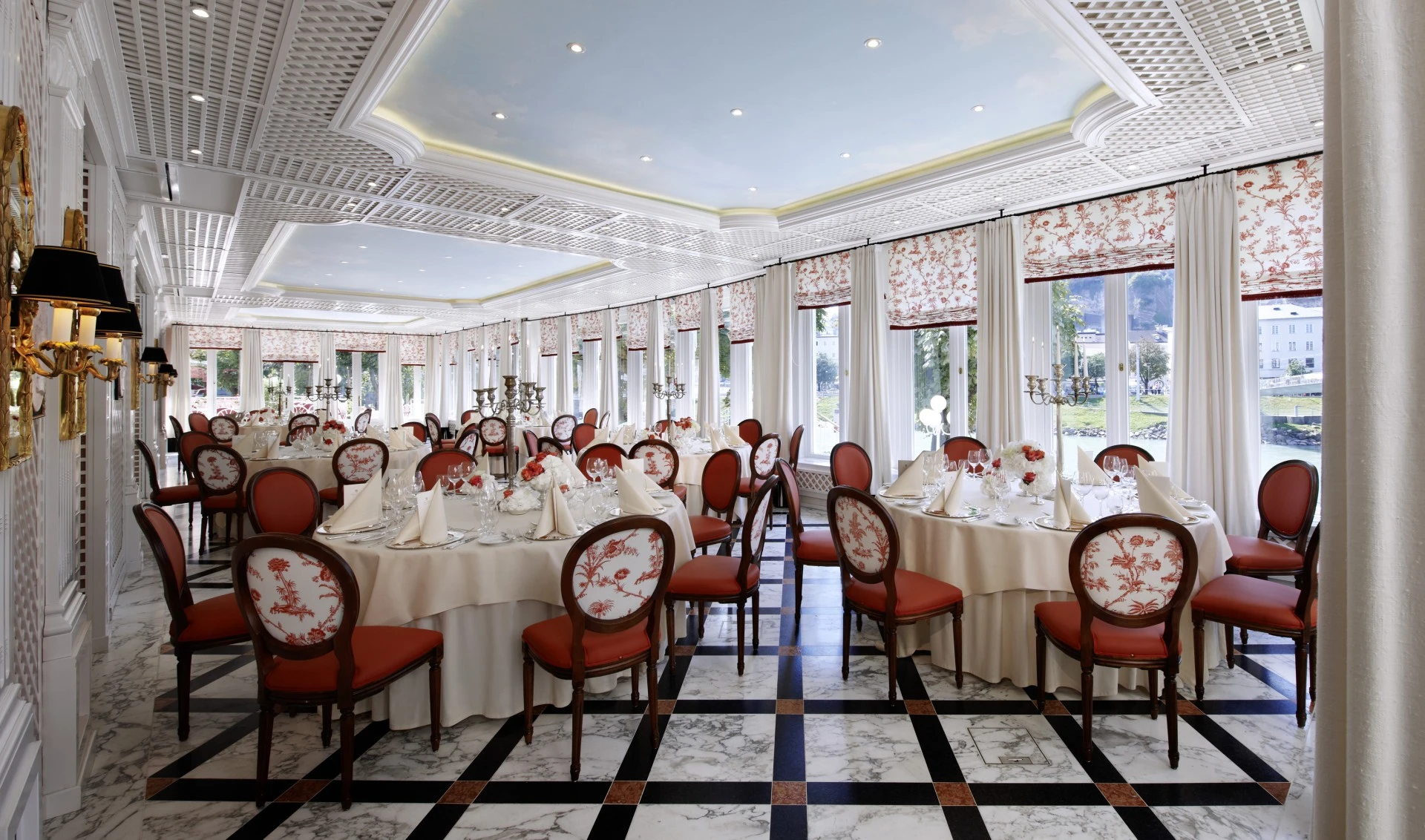 Banquet room at Hotel Sacher Salzburg with marble flooring, round tables, floral centrepieces, and elegant ceiling details.