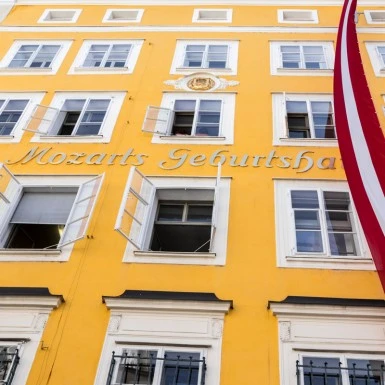 This image shows Mozart's Birthplace in Salzburg, Austria, a bright yellow historic building marked with the words 