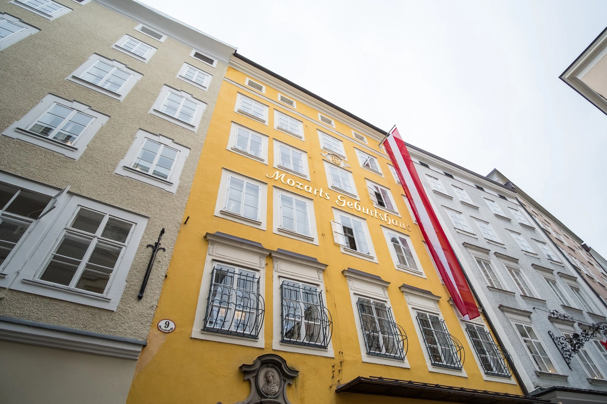 This image shows Mozart's Birthplace in Salzburg, Austria, a bright yellow historic building marked with the words 