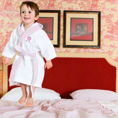 Child standing on a bed in a luxury bathrobe at Petit Sacher, Hotel Sacher's family-friendly accommodations.