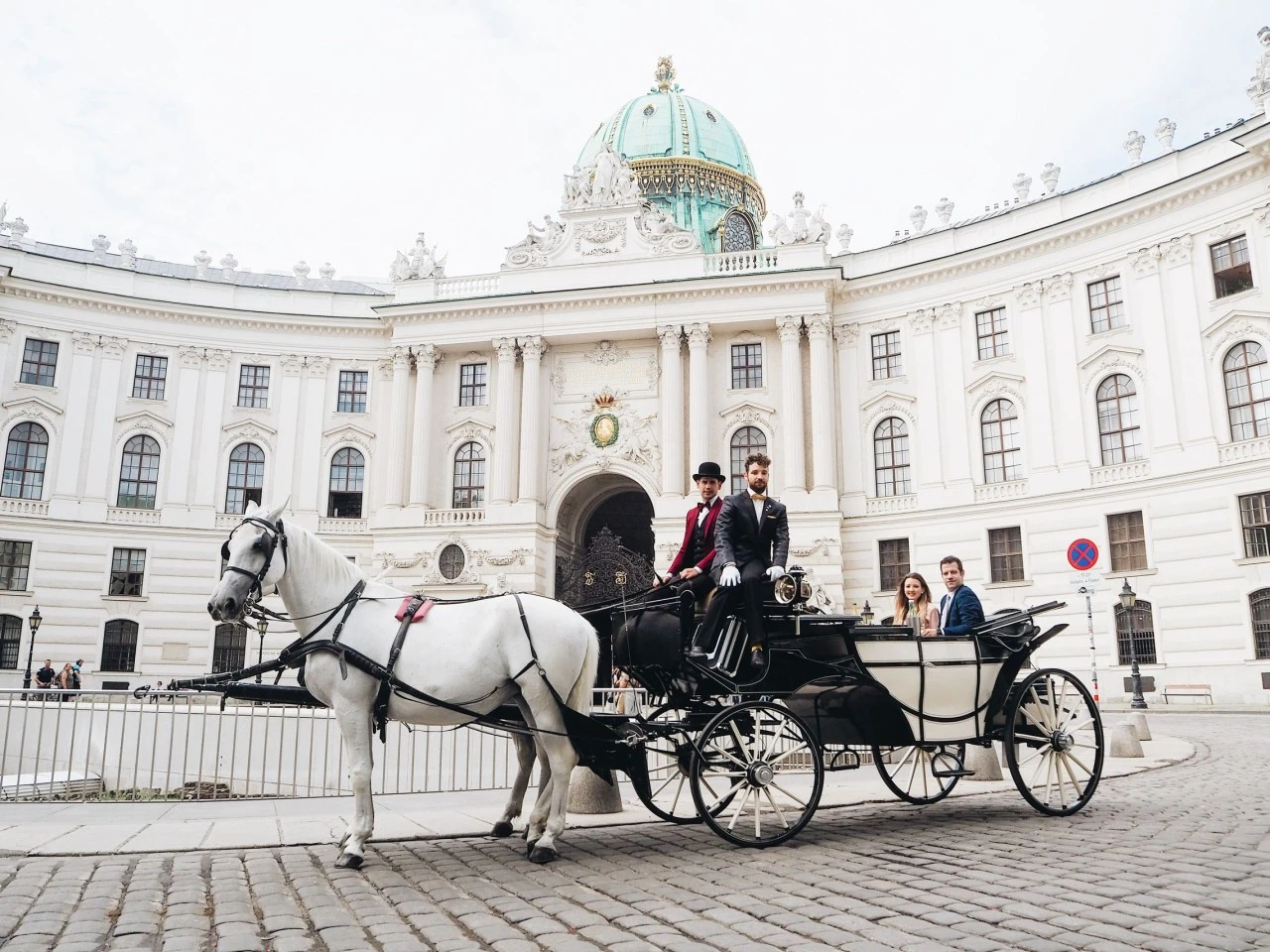 Horse-drawn carriage with guests in front of Vienna's Hofburg Palace, offering a classic sightseeing experience.