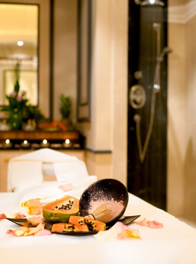 A serene Sacher Spa treatment room adorned with rose petals and candlelight, featuring fresh papaya and a ceramic bowl with spa ingredients for a luxurious, nature-inspired wellness ritual.