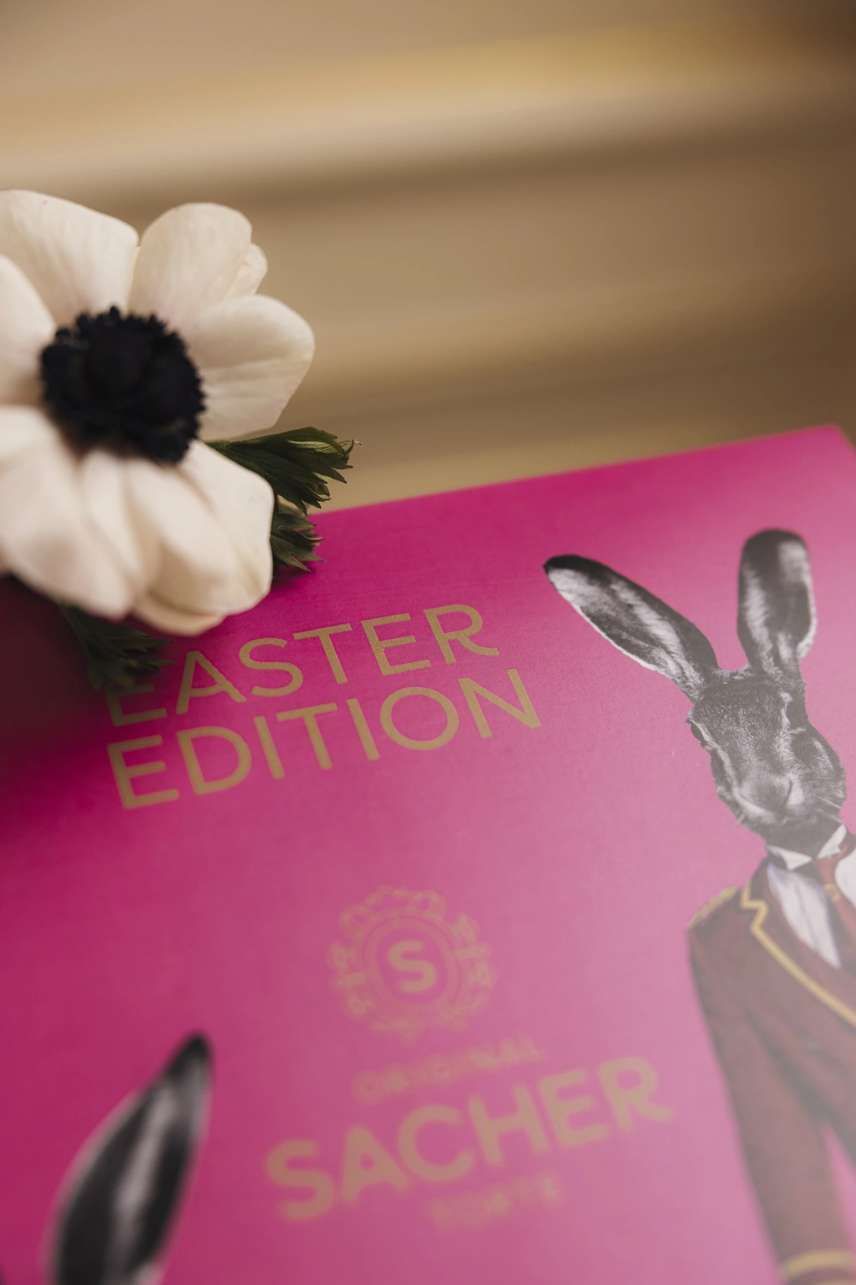 A close-up of the vibrant pink Easter Edition box of the Original Sacher-Torte, decorated with a whimsical illustration of a rabbit in uniform and complemented by a delicate white flower.