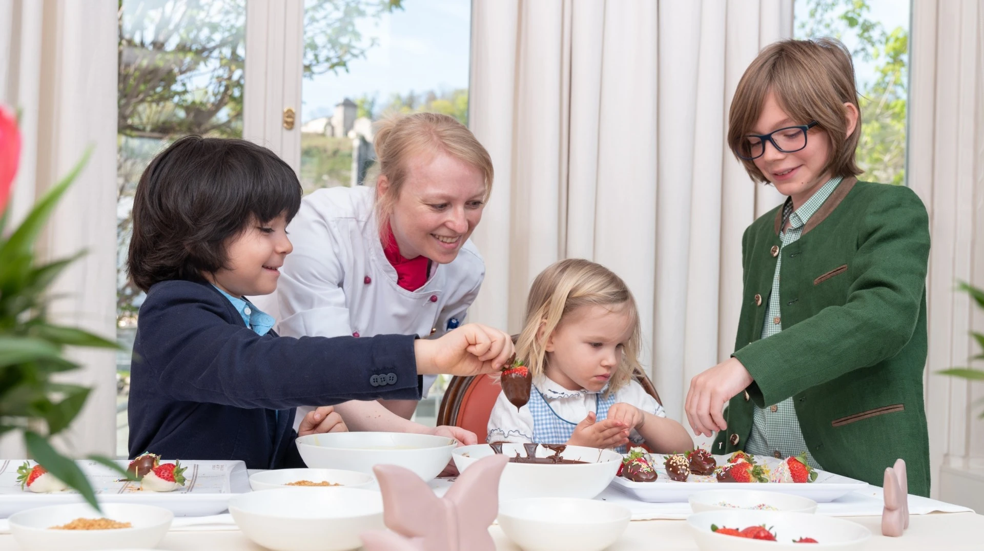 A sweet moment of joy as children dip strawberries in chocolate, guided by a smiling chef in a warm and elegant setting.