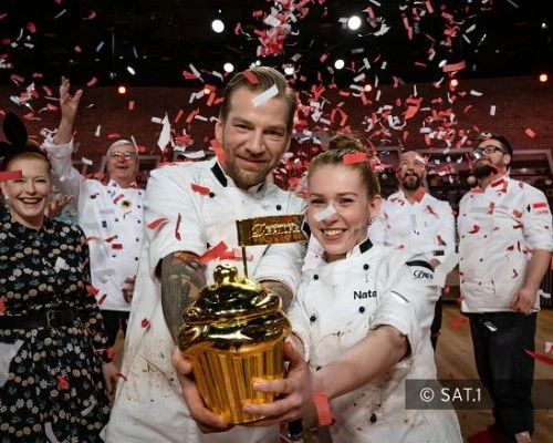 With confetti raining down, the winning pastry team beams with joy as they proudly hold their golden trophy.