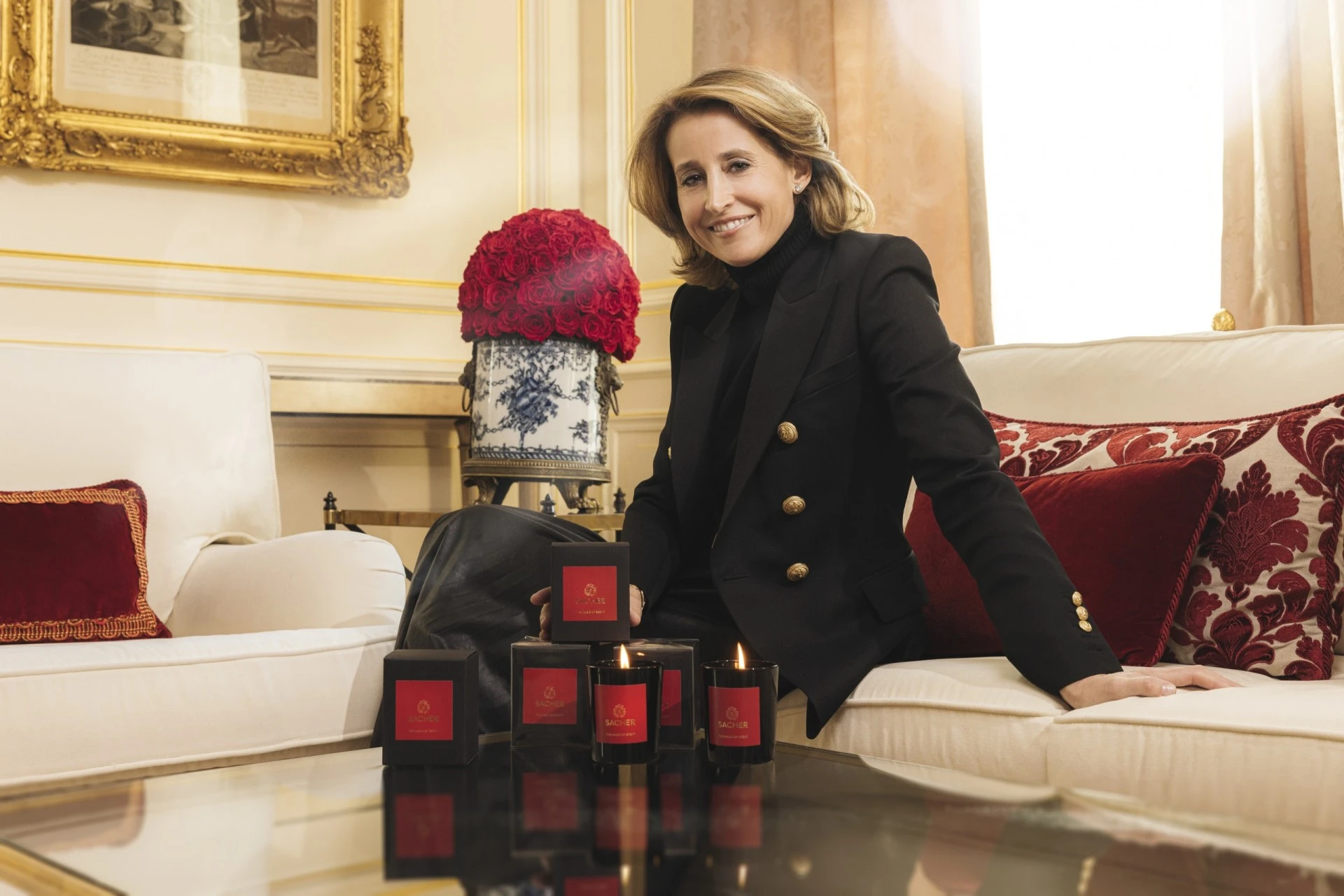 Alexandra Winkler sits gracefully in an elegant, warmly lit room, holding a Sacher candle box in her hands while surrounded by glowing candles and beautifully stacked packaging, embodying refined luxury and calm.