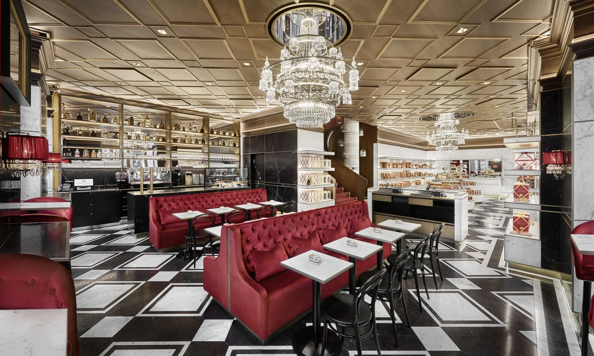 This is Sacher Eck Wien, an opulent and modern Viennese café with plush red seating, marble tables, grand chandeliers, and shelves lined with elegantly packaged Sacher delights.