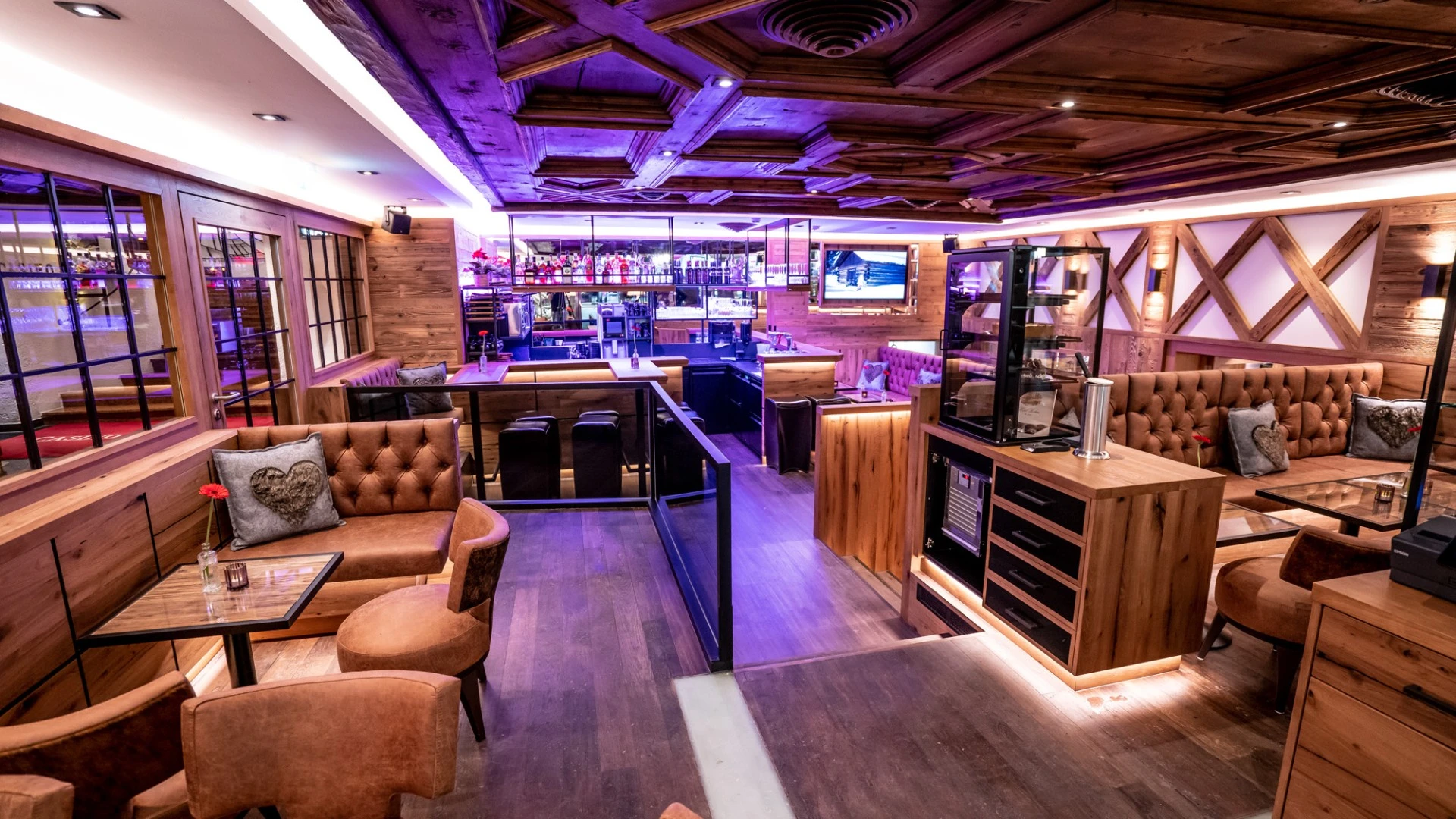 This is a cozy and stylish wooden lounge bar with soft leather seating, warm lighting, and a glowing bar area at the back.