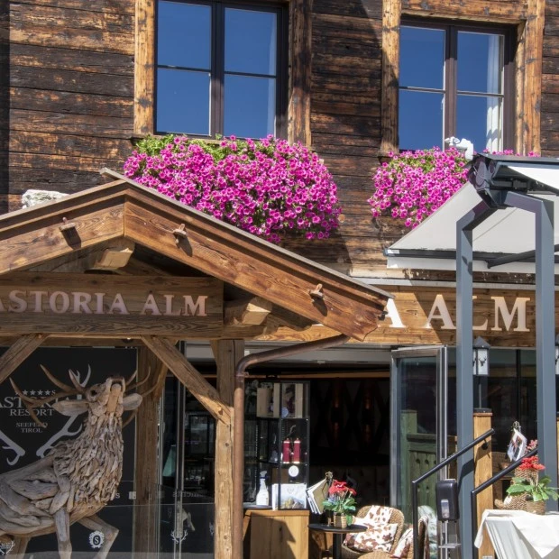 The charming entrance of Astoria Alm in Seefeld, Tirol features rustic wooden architecture, vibrant flower boxes, and alpine-inspired decor, warmly inviting guests into its cozy mountain ambiance.