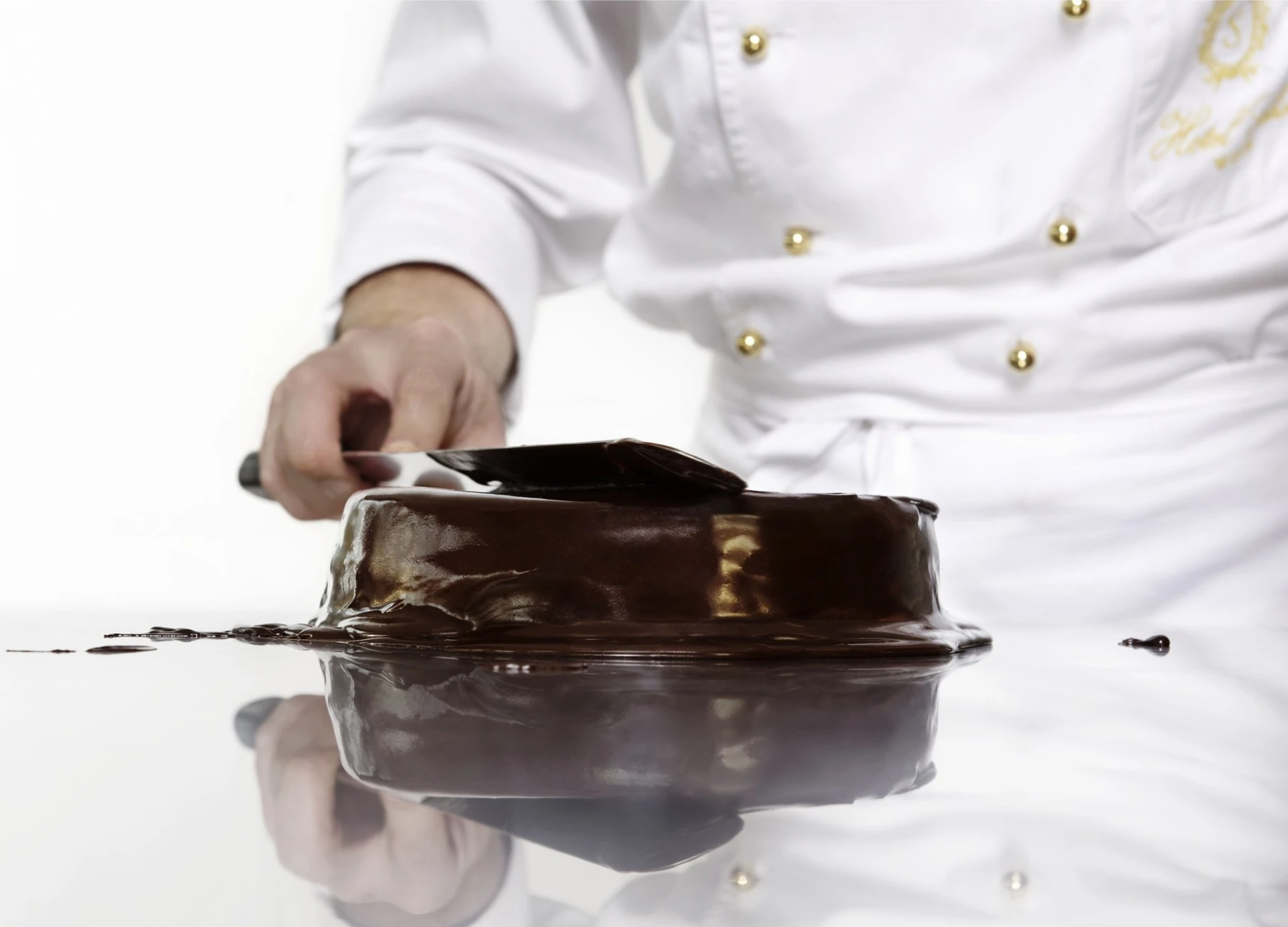 A pastry chef in a crisp white uniform expertly coats the iconic Original Sacher-Torte in a glossy layer of rich chocolate glaze.