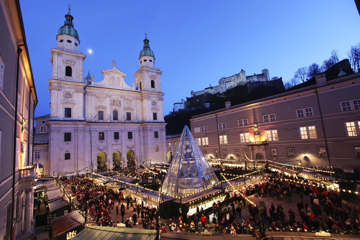 The Salzburg Christmas Market glows with festive charm in the shadow of the Salzburg Cathedral and Hohensalzburg Fortress, as crowds enjoy the twinkling lights, cozy stalls, and holiday spirit.