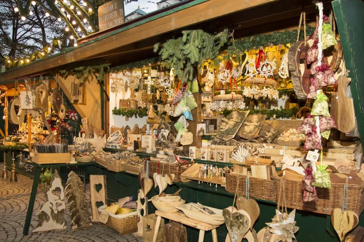 A cozy Christmas market stall in Salzburg overflows with handcrafted wooden decorations, ornaments, and festive trinkets, glowing warmly under twinkling string lights and pine garlands.