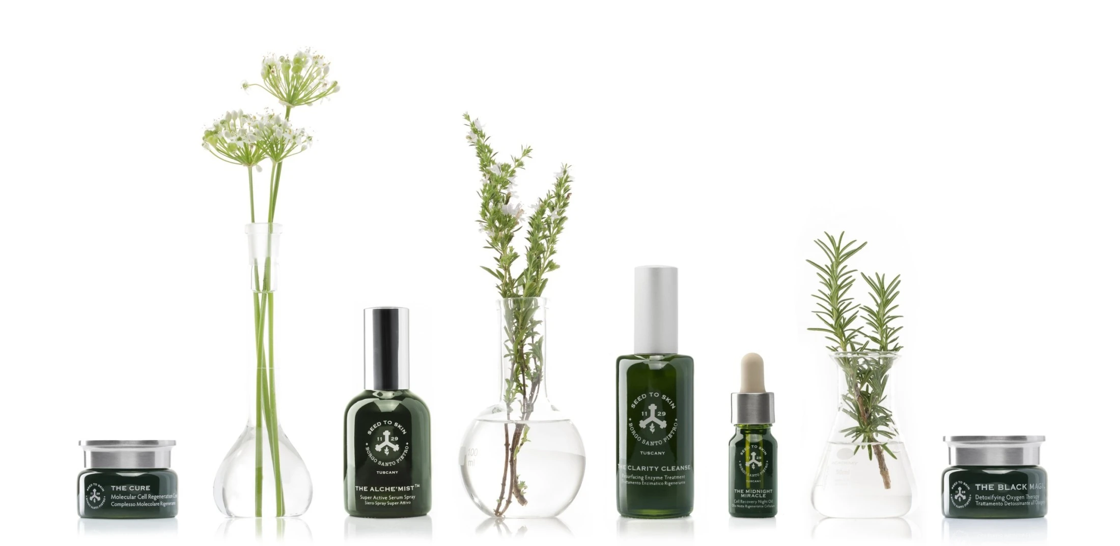A luxurious lineup of Seed to Skin Tuscany skincare products is elegantly displayed alongside fresh botanical elements in glass lab vessels, emphasizing a natural and scientific approach to beauty.