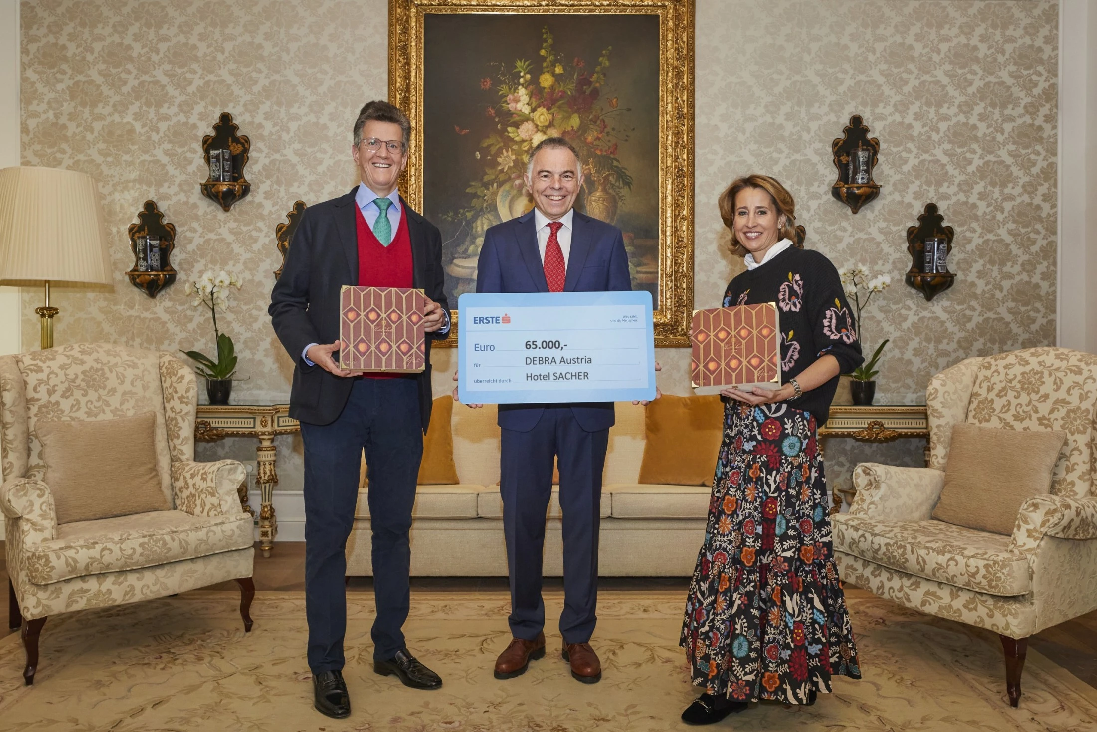 Georg Gürtler and Alexandra Winkler proudly present a €65,000 donation from Hotel Sacher to DEBRA Austria, each holding a beautifully designed box of the **Original Sacher-Torte**, symbolizing the brand’s commitment to both tradition and social responsibility.